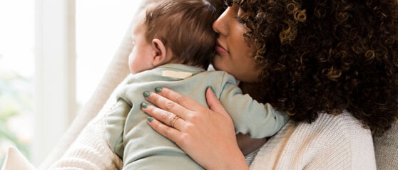 woman with curly hair holding baby near a window