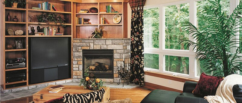 living room with built-in shelves and stone fireplace and wall of windows